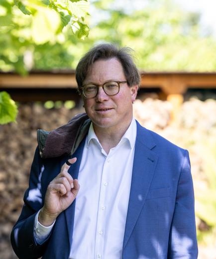 Mann mit Brille bis zur Taile sichtbar mit blauen Jackett schaut in die Kamera.
